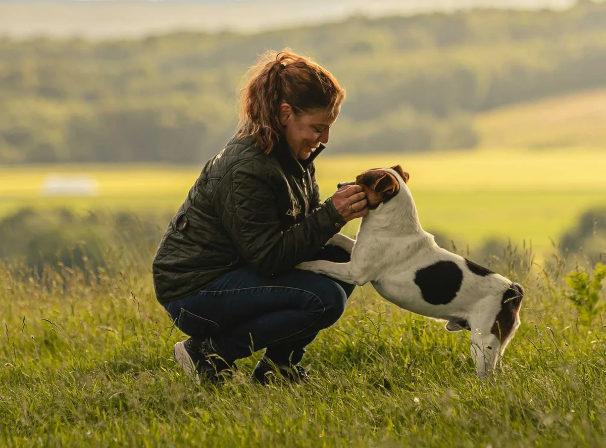 Hundägare knäböjer och interagerar med sin valp på fält